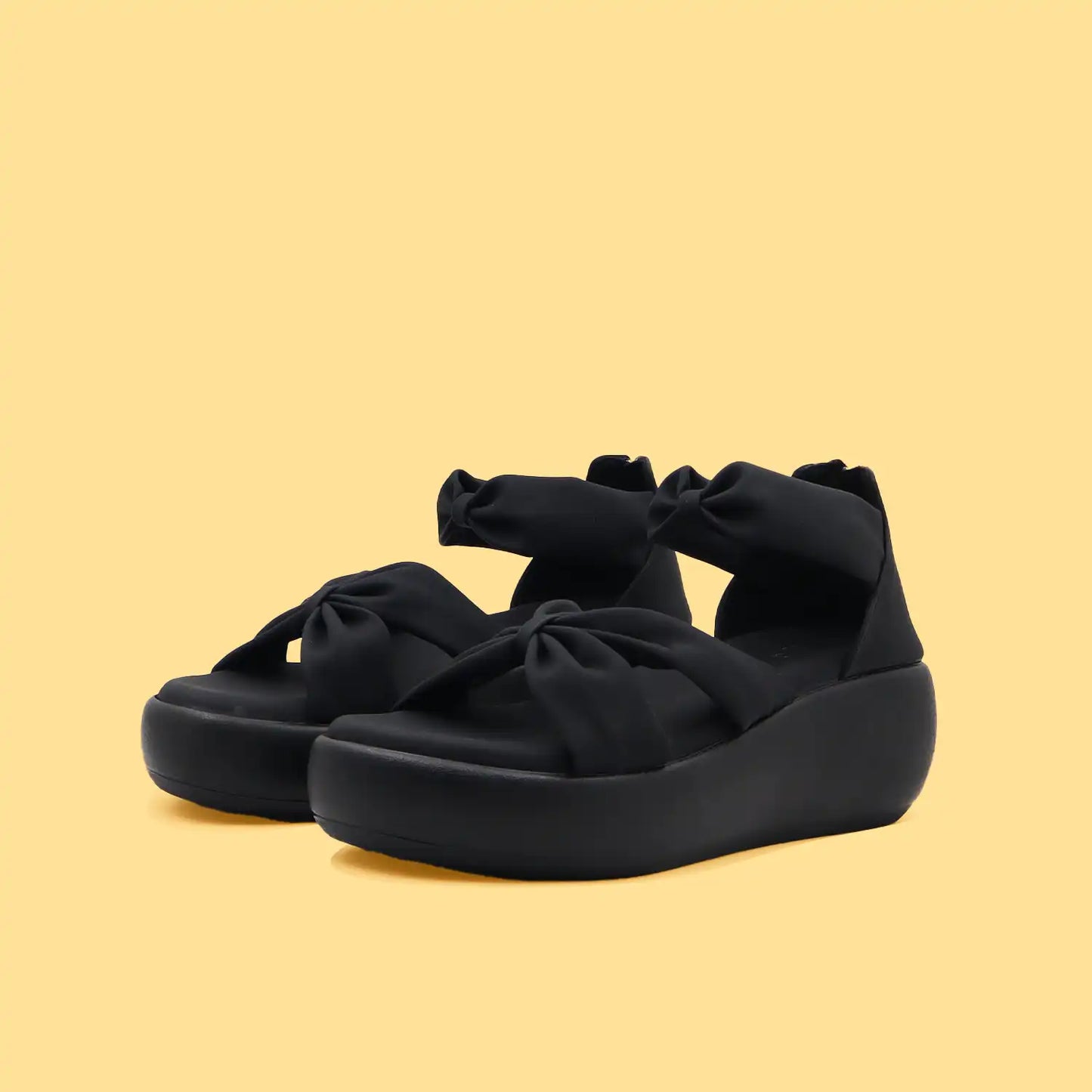 Women's black platform heel sandals with bow details on a yellow background