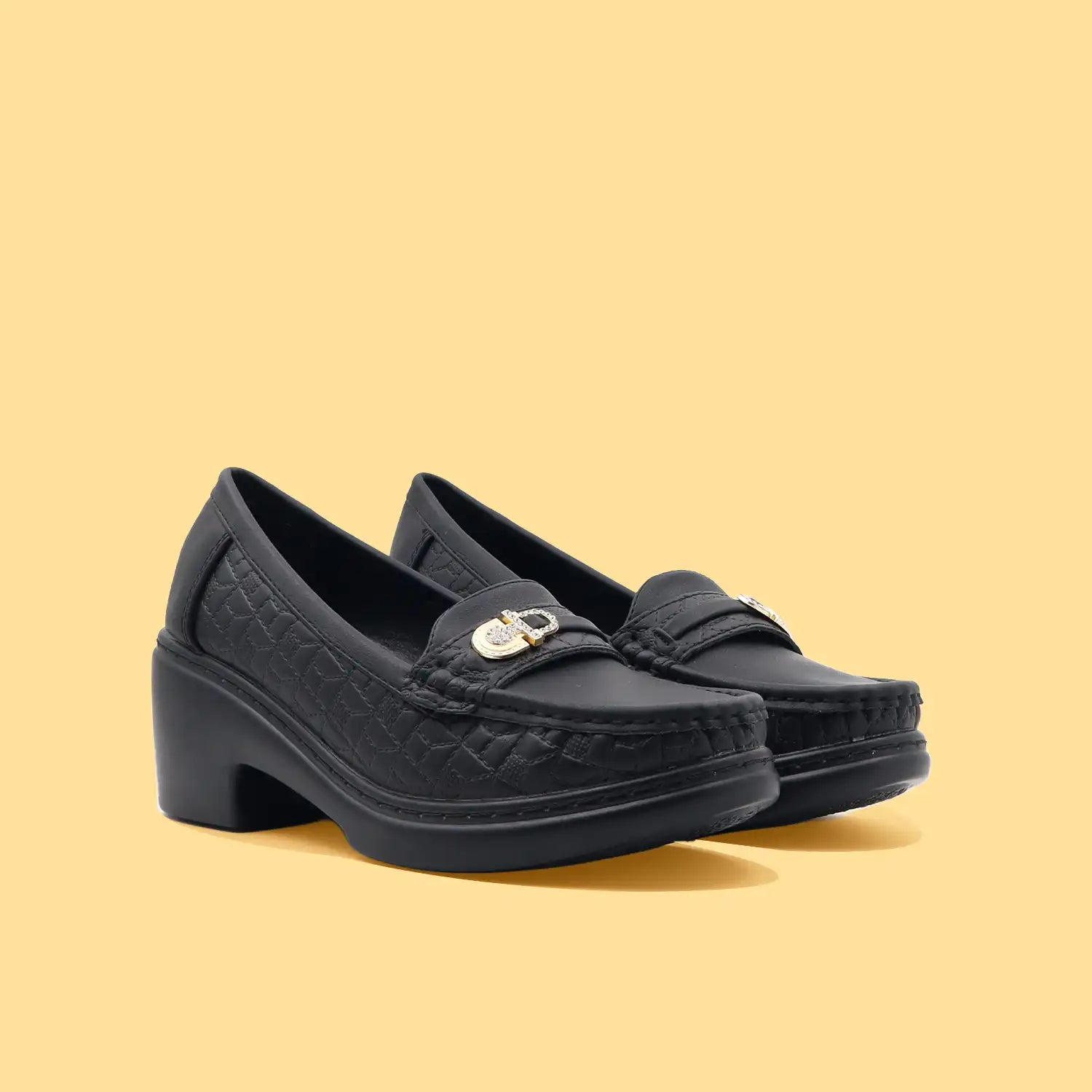 Pair of black loafers with a gold buckle on a beige background