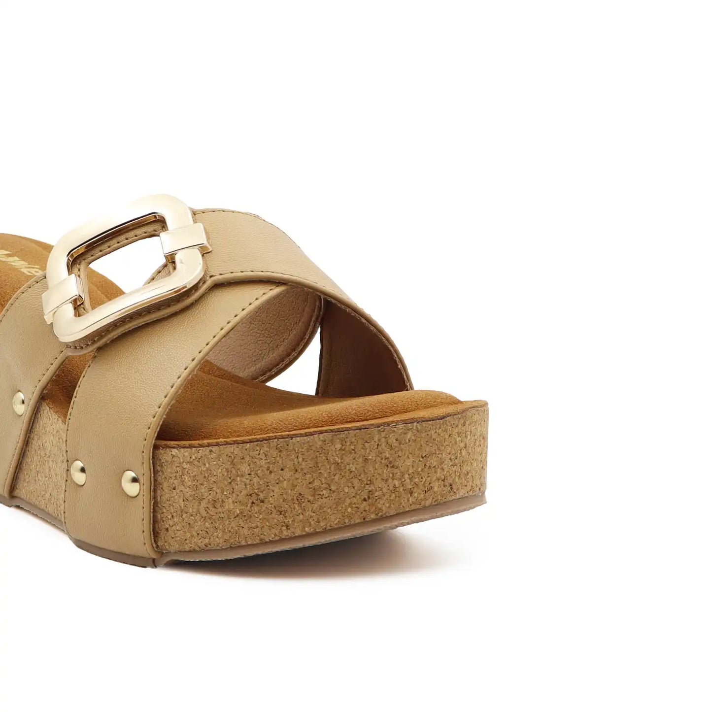 A close-up of a platform slide sandal featuring a wide tan strap with a large gold-tone buckle, a cork-textured platform sole, and small gold-tone studs on a white background.