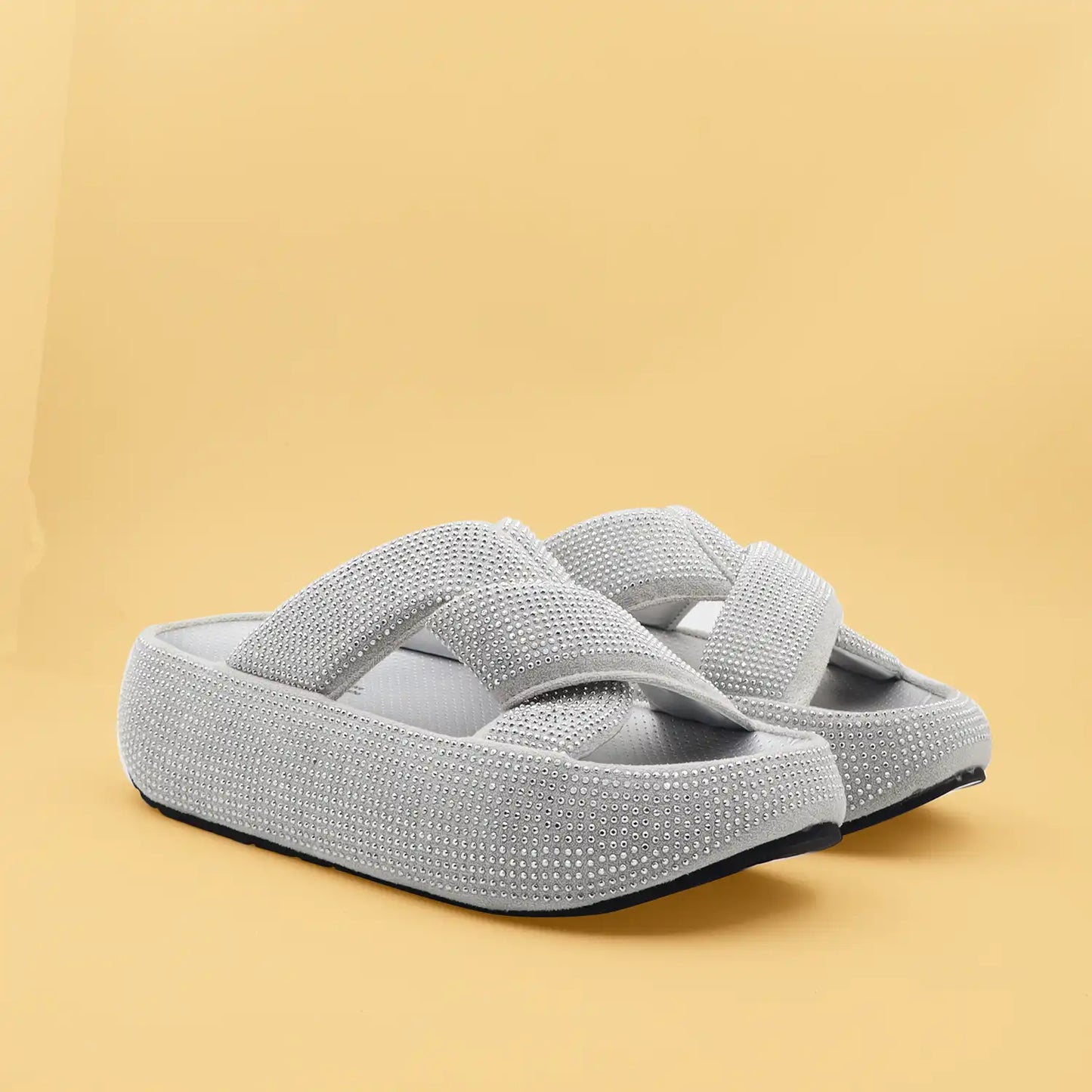 A pair of light gray platform slide sandals embellished with sparkling rhinestones, set against a solid warm beige background.