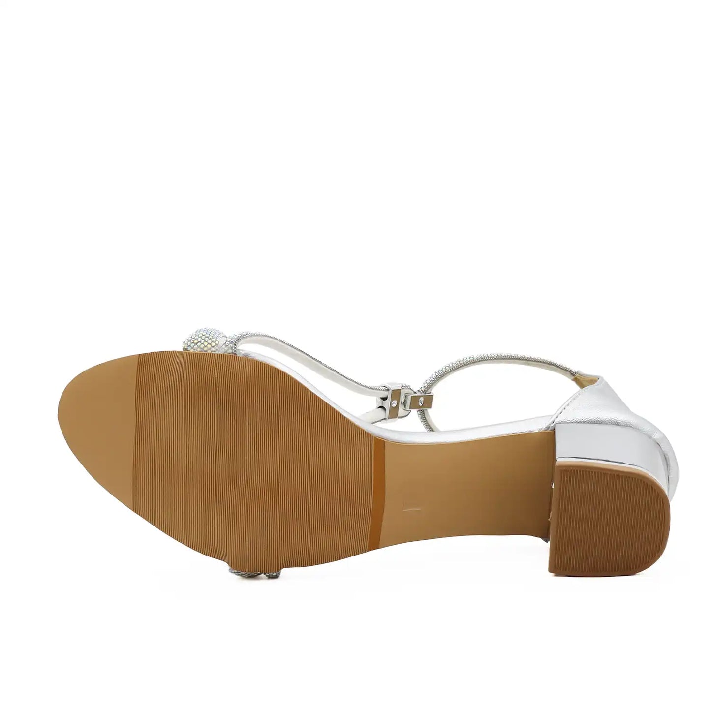 A single women's heeled sandal shown from the sole view, featuring a metallic silver T-strap with a rhinestone embellishment, a tan textured outsole, and a brown block heel, set against a plain white background.